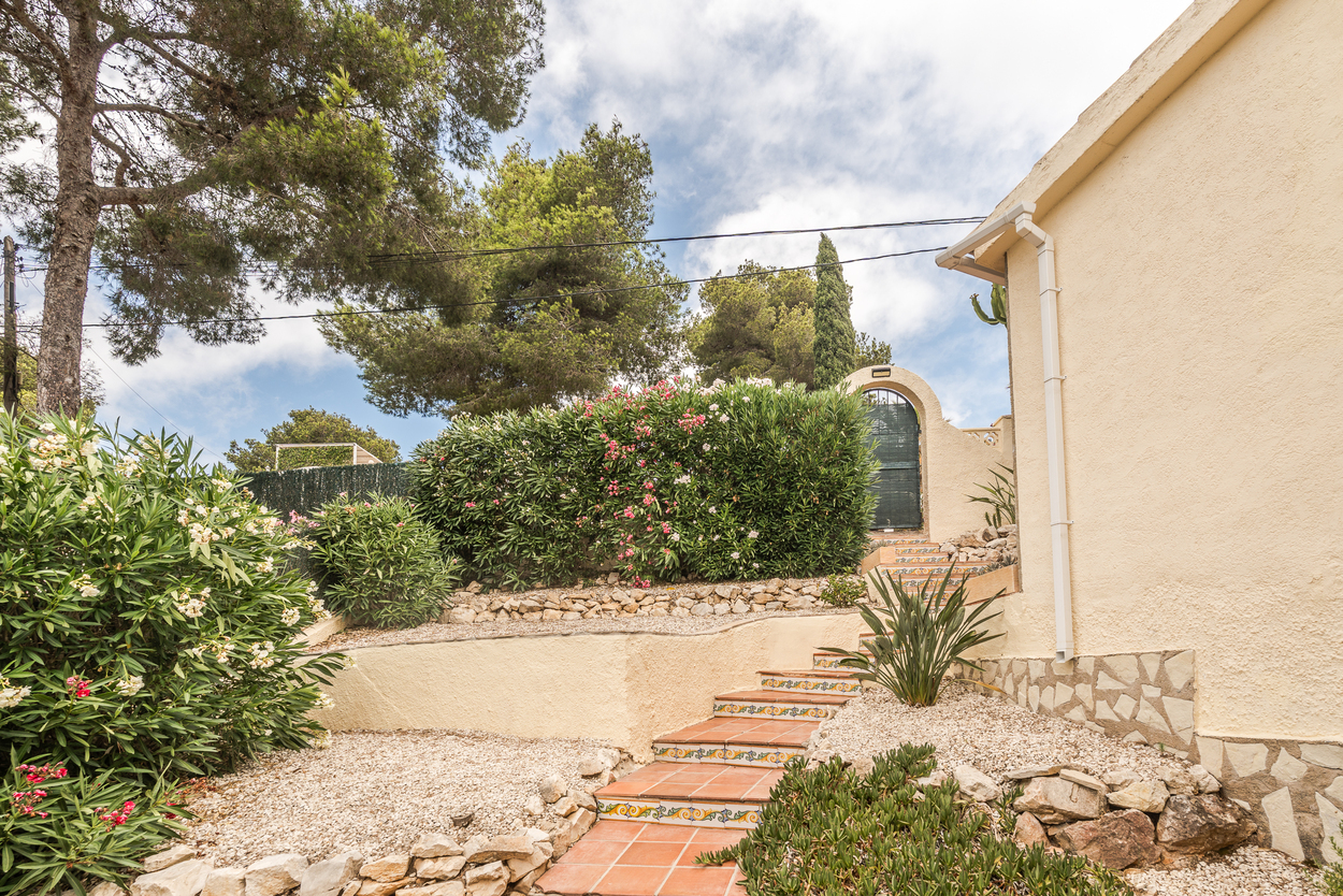 Jardin méditerranéen en terrasses avec escaliers en terre cuite, contremarches décorées et gravier blanc, menant à un portail voûté entouré de lauriers-roses.