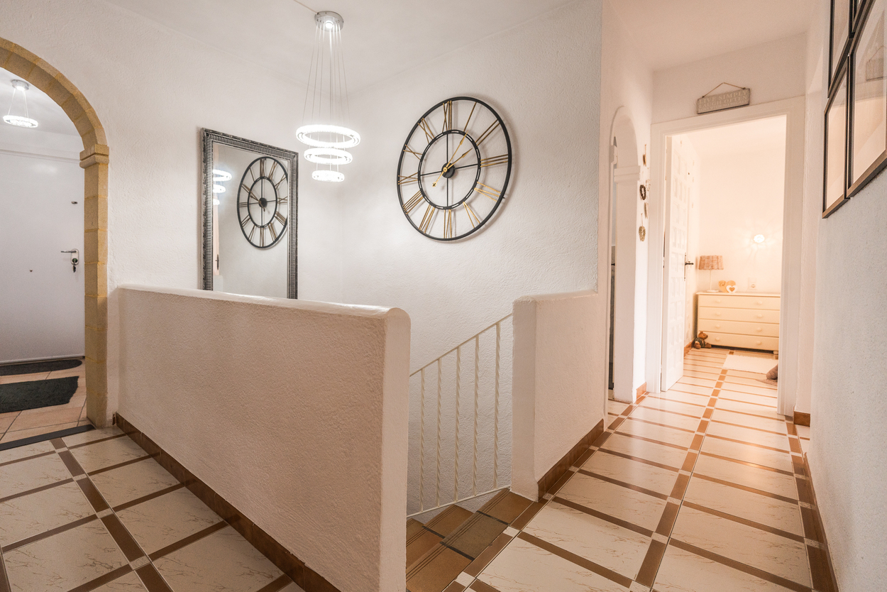 Palier d'étage avec arche en pierre de Tosca, sol en carrelage à motifs géométriques et lustre LED moderne surplombant l'escalier intérieur.