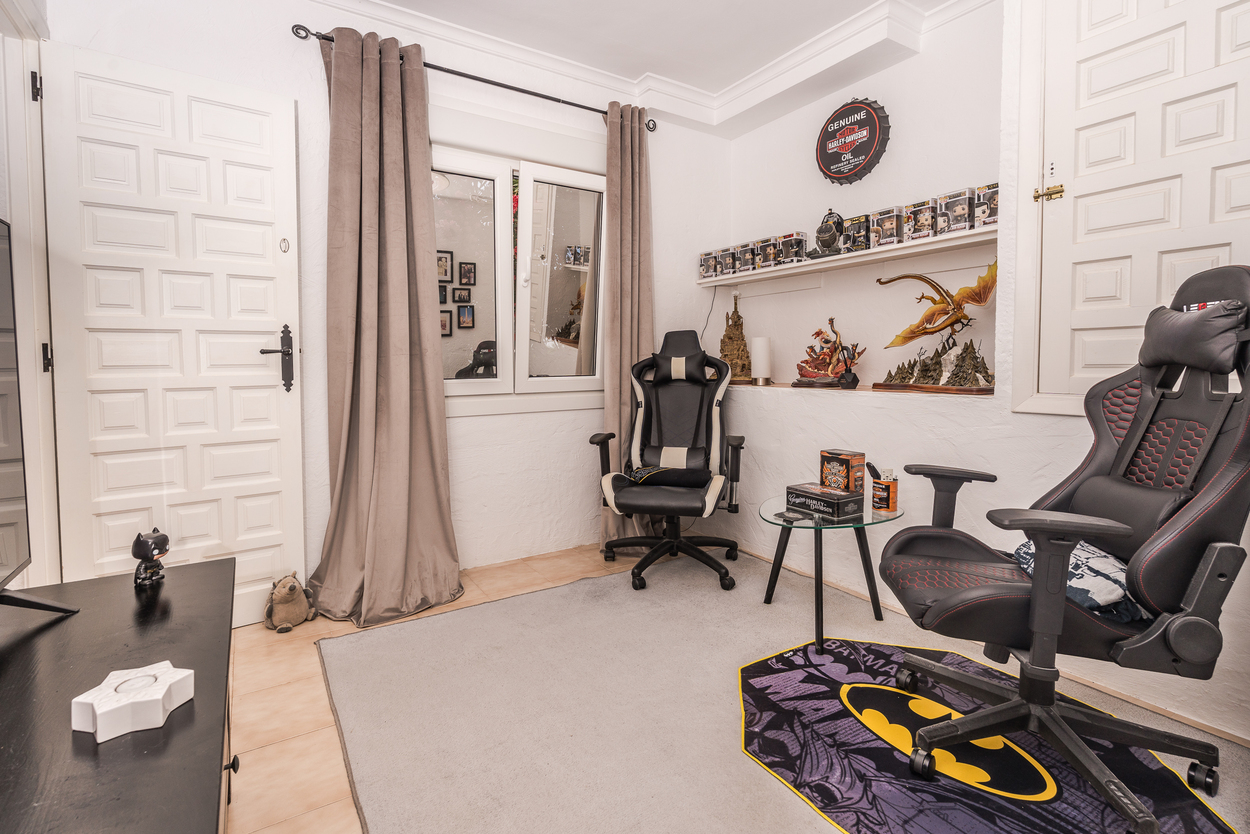 Pièce de loisirs moderne avec chaises de gaming, étagères intégrées et fenêtres à double vitrage. Le sol est en carrelage avec des portes blanches sculptées.