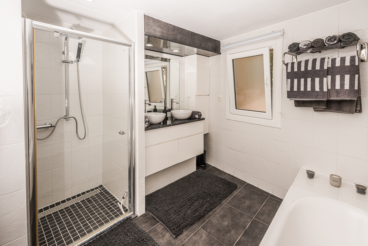 Salle de bain moderne avec douche à l'italienne vitrée, double vasque sur plan de travail sombre et carrelage au sol anthracite.