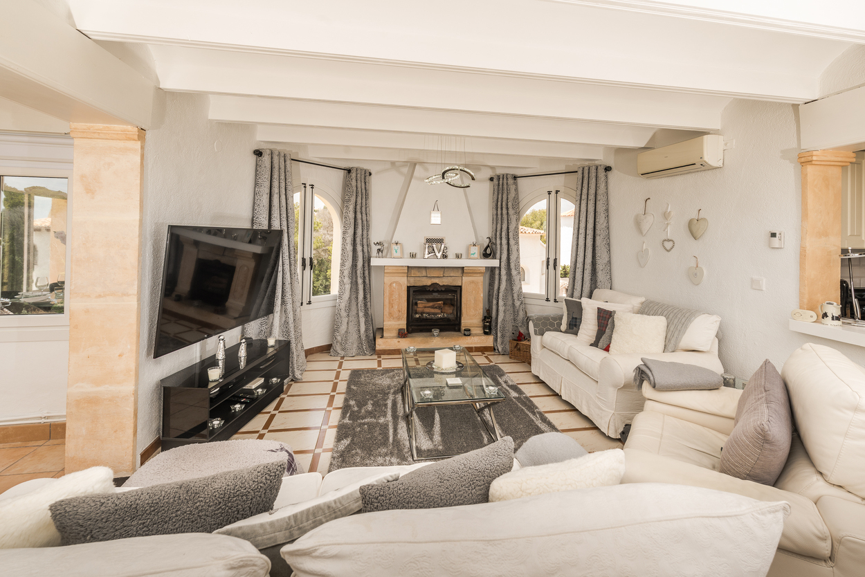 Salon lumineux avec cheminée en pierre Tosca, plafonds à poutres blanches, piliers en pierre naturelle et carrelage traditionnel.