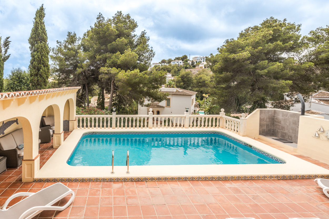 Terrasse extérieure avec piscine de 8x4m, balustrade blanche et naya couverte à arcades, entourée de pins matures dans un cadre méditerranéen préservé.