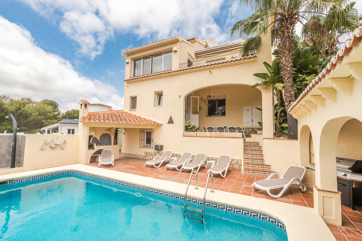 Vue extérieure de la piscine 8x4m et de la terrasse en terre cuite, comprenant un espace barbecue couvert, des transats et une naya voûtée pour les repas.
