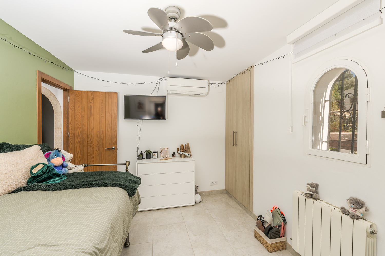 Chambre lumineuse avec mur d'accent vert, placards intégrés et fenêtre en arche. Équipée d'un ventilateur de plafond, de la climatisation et d'un radiateur.