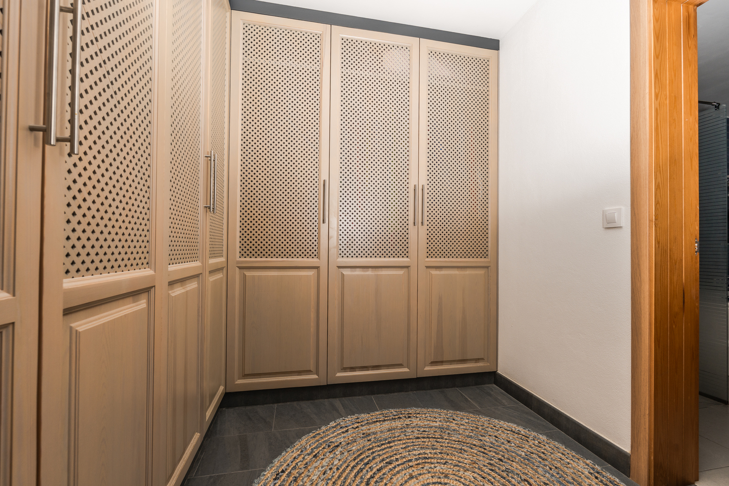 Dressing avec placards intégrés en bois clair et panneaux en treillis, sol en carrelage sombre et tapis circulaire en jute.