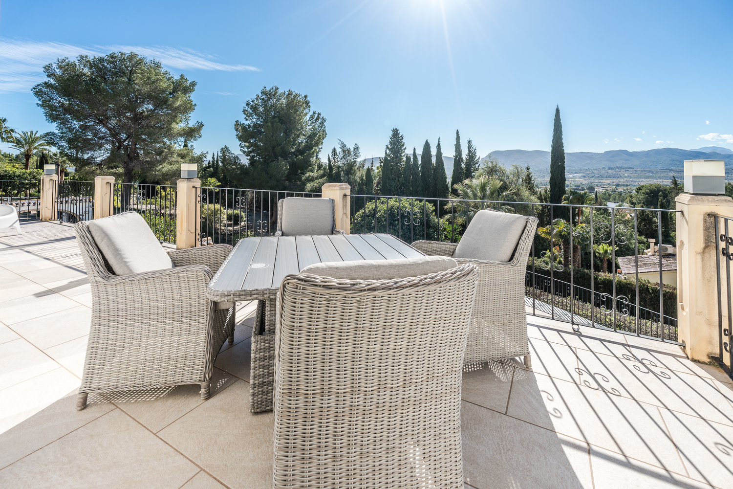 Grande terrasse extérieure avec mobilier en résine tressée et vue panoramique sur la vallée. Le sol est en dalles de pierre claire avec une rambarde en fer forgé.