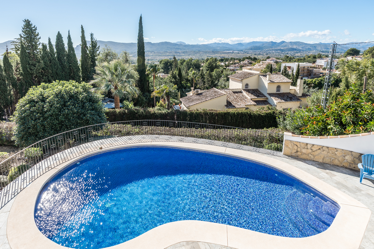 Piscine en forme de rein avec mosaïque bleue, entourée d'une terrasse en pierre et d'une balustrade en fer forgé, offrant une vue panoramique sur la vallée.
