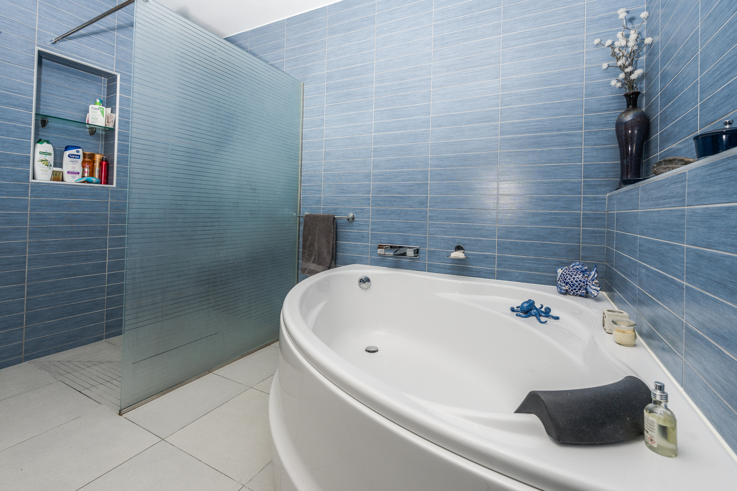 Salle de bain moderne avec baignoire ovale et douche à l'italienne, paroi en verre dépoli, carrelage mural bleu texturé et sol en grès cérame gris clair.