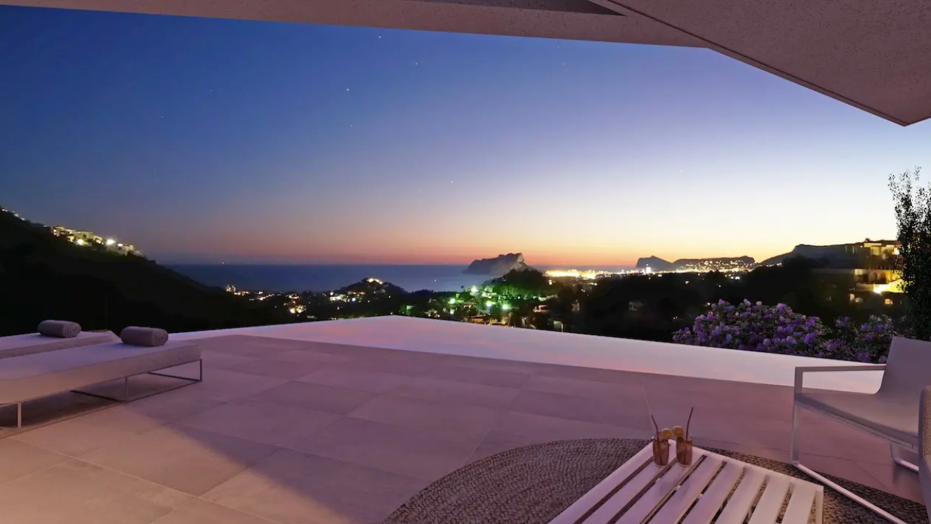 Terrasse avec piscine à débordement offrant une vue panoramique sur la côte au crépuscule. Comprend un sol en dalles grand format et du mobilier d'extérieur moderne.