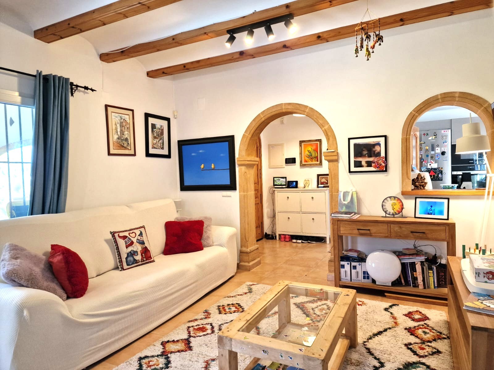 Salon avec poutres en bois apparentes, arches en pierre de Tosca traditionnelle et un agencement lumineux communiquant avec la cuisine par une ouverture voûtée.