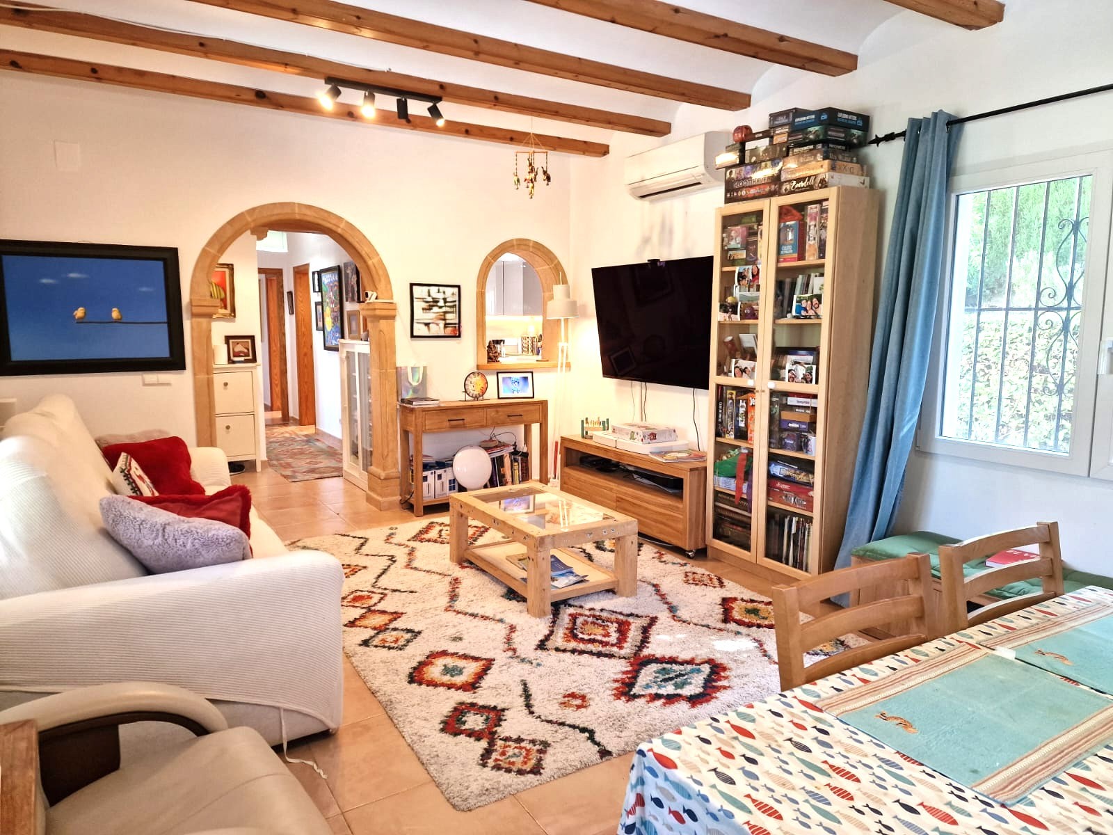 Salon et salle à manger avec poutres en bois apparentes, arches en pierre de Tosca et climatisation. L'espace comprend un coin séjour et un accès vers la cuisine.