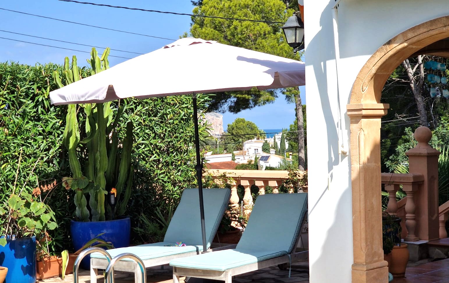 Terrasse avec chaises longues et parasol près d'une arche en pierre, entourée de plantes méditerranéennes avec une vue dégagée sur la mer et le Cabo de San Antonio.