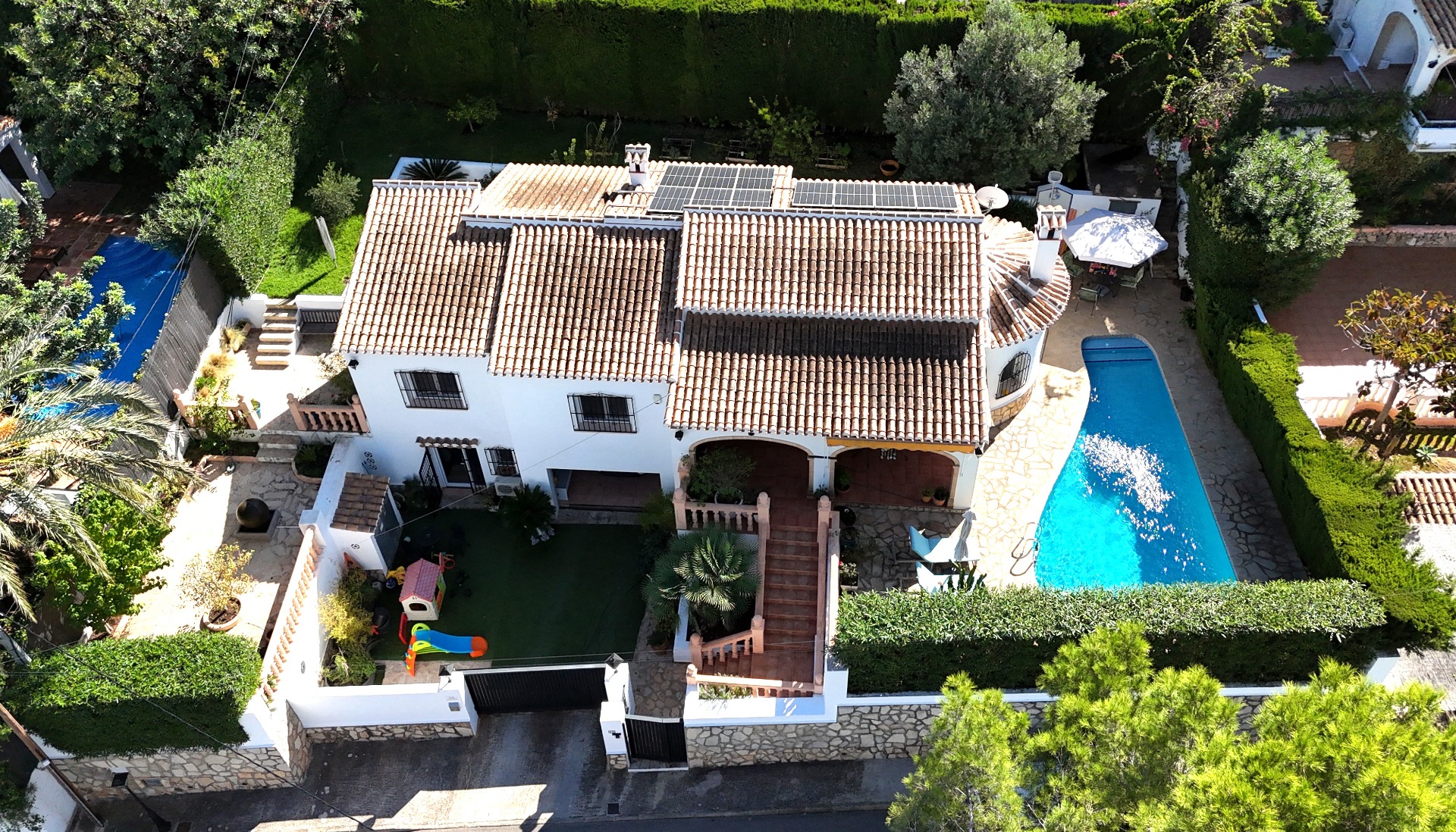 Vue aérienne de cette villa à Toscal avec toit en terre cuite, panneaux solaires, piscine privée et aire de jeux pour enfants dans un jardin paysager.