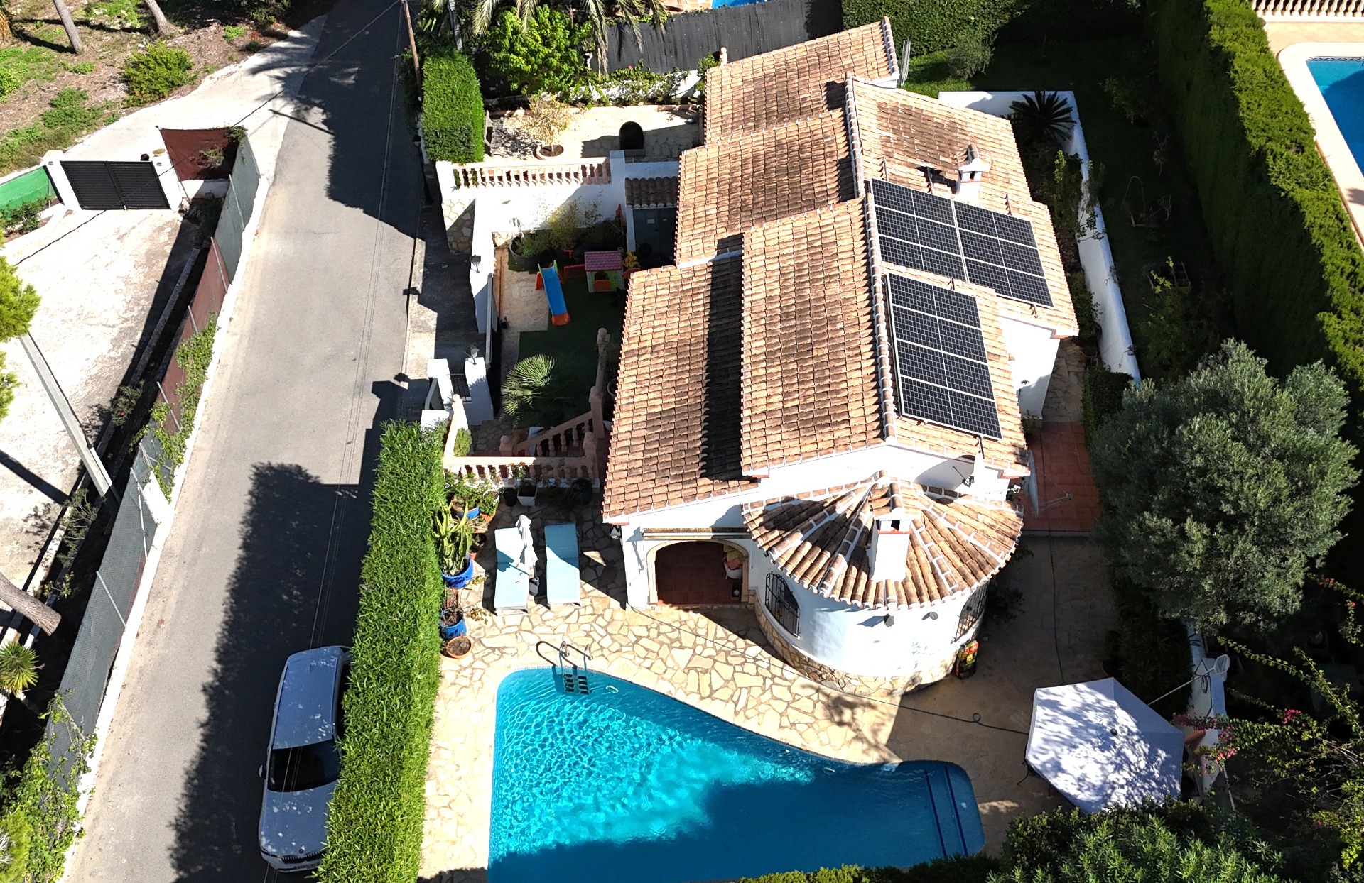 Vue aérienne de la villa avec piscine privée, panneaux solaires sur le toit en terre cuite et aire de jeux pour enfants dans le jardin clos.