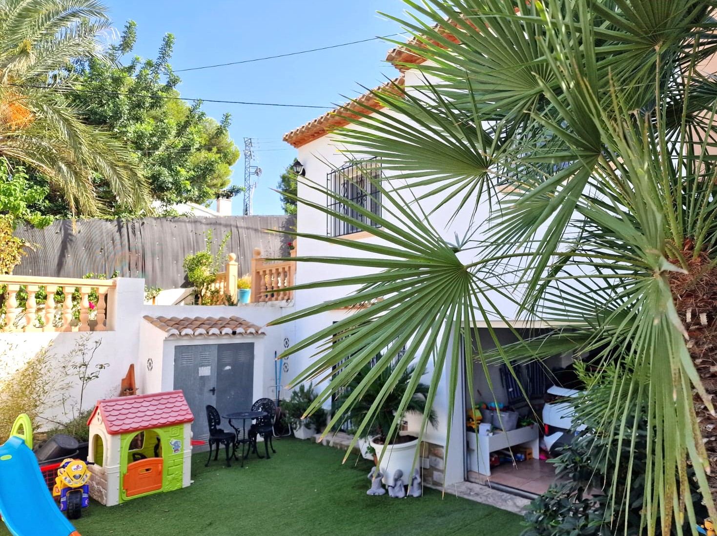 Vue extérieure du niveau inférieur avec une aire de jeux pour enfants sur gazon synthétique, un abri de rangement et l'entrée du garage ouvert.