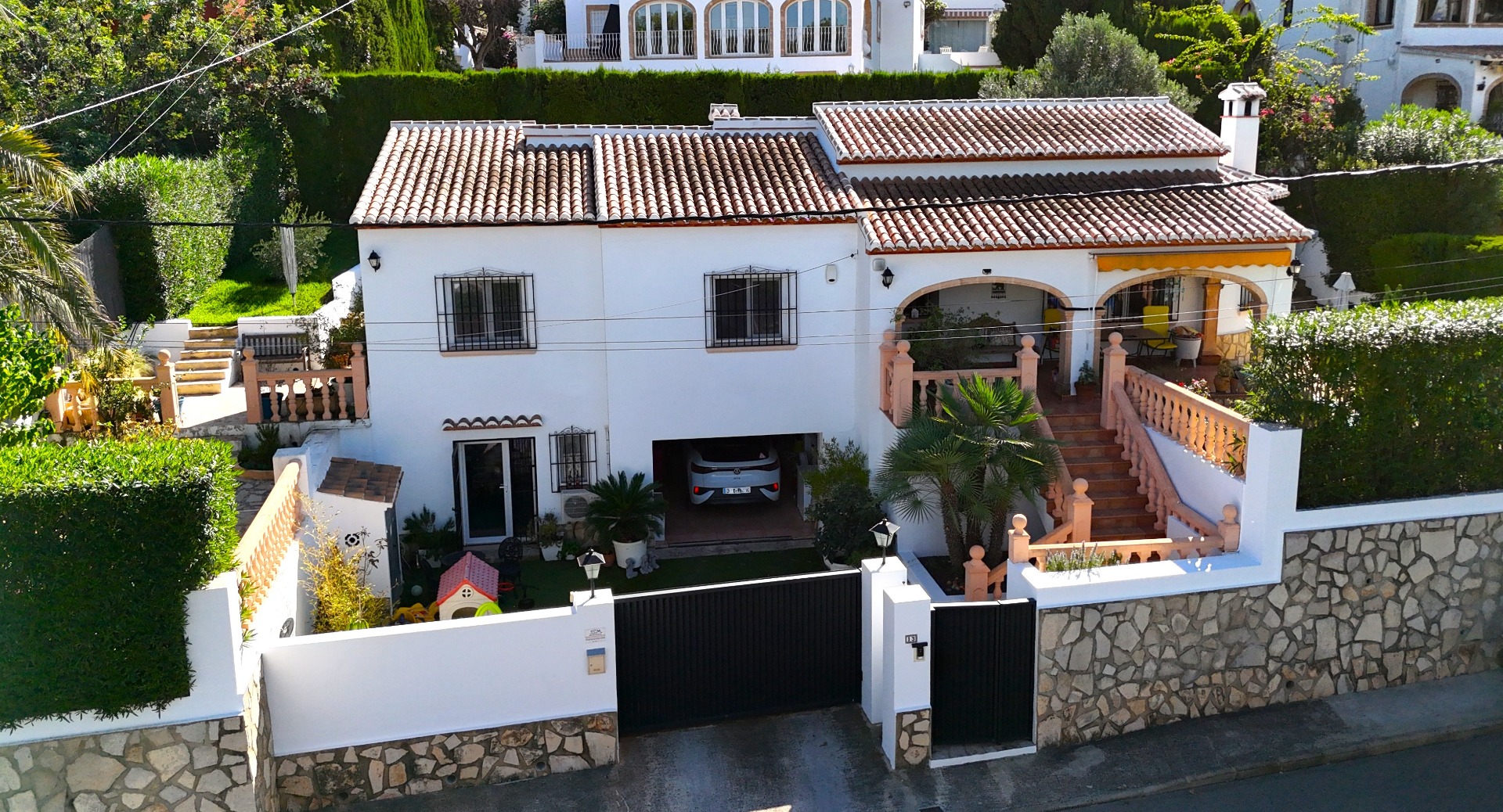 Vue extérieure d'une villa méditerranéenne sur deux niveaux avec façade blanche, toit en terre cuite, garage intégré et terrasse voûtée avec balustrades.