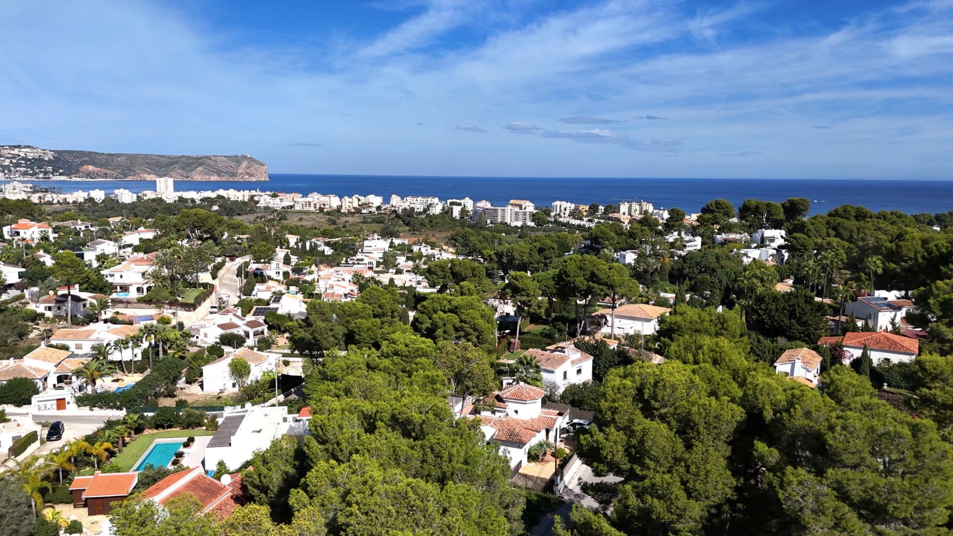 Vue panoramique sur le quartier résidentiel du Toscal à Jávea, présentant des villas méditerranéennes entourées de pins avec le Cabo de San Antonio à l'horizon.