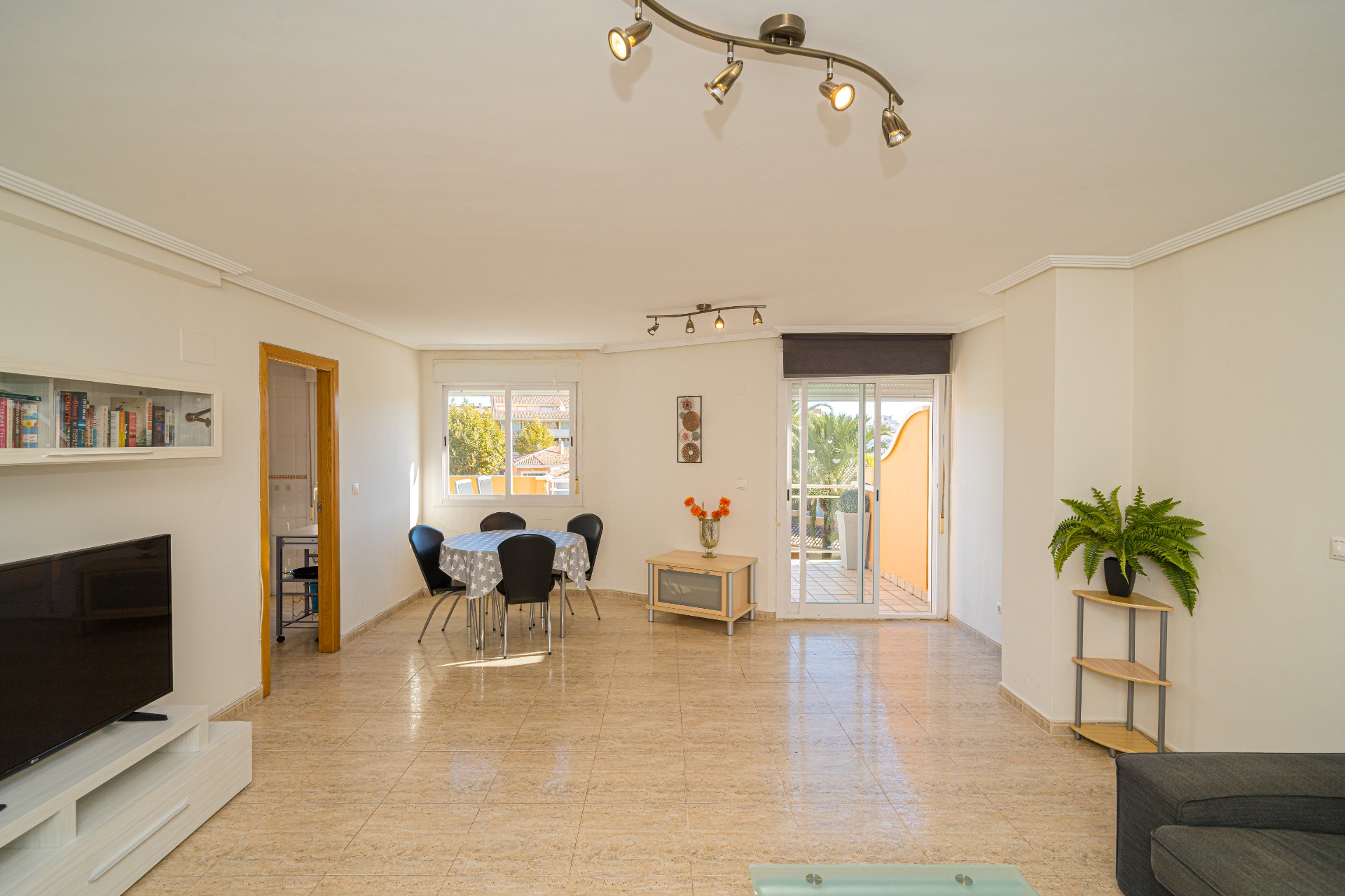 Salon-salle à manger spacieux avec sol en grès cérame, éclairage sur rail et accès direct à une terrasse privée par des baies vitrées coulissantes.