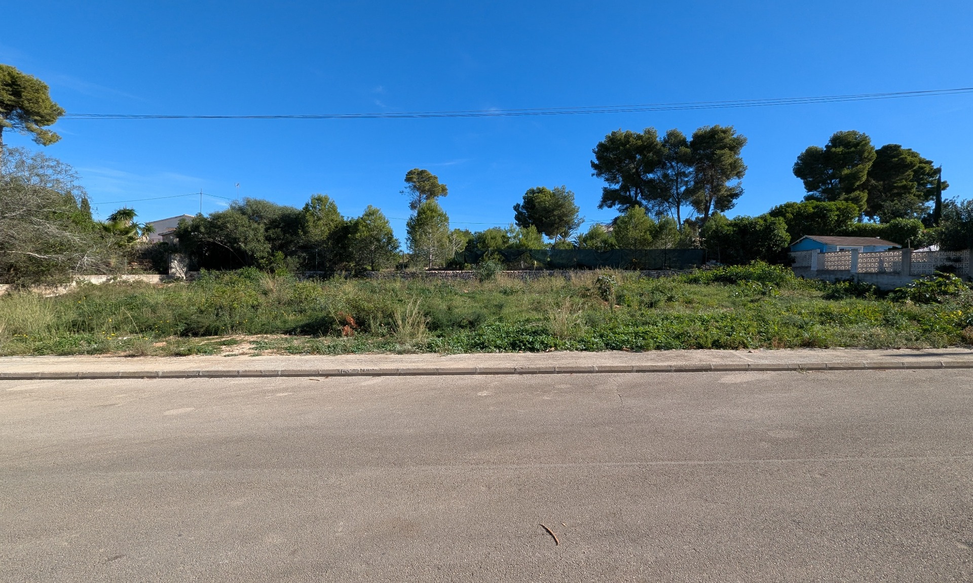 Terrain plat de 889 m² à Pinosol, Jávea, offrant une large façade sur rue, une végétation méditerranéenne environnante et une surface nivelée prête à bâtir.