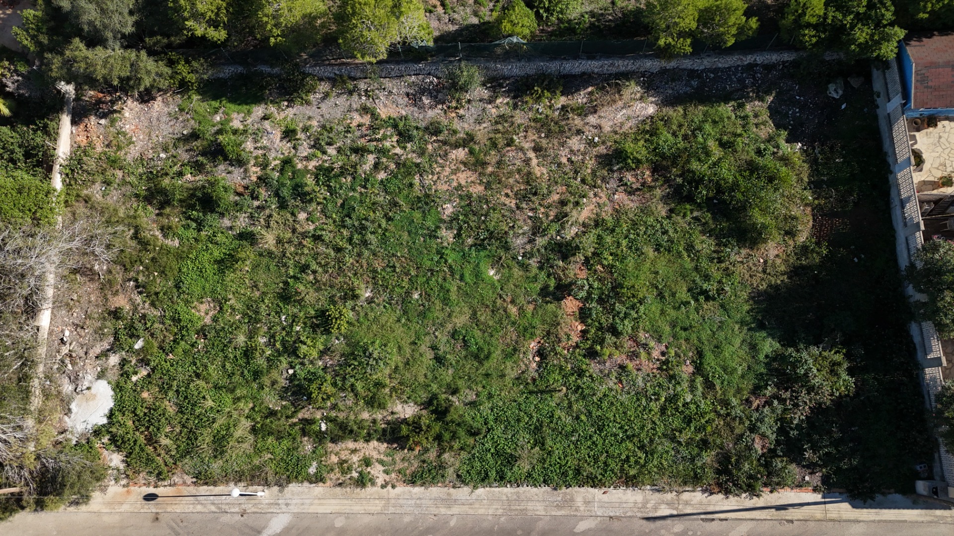 Vue aérienne du terrain plat de 889 m² à Pinosol, illustrant sa configuration rectangulaire, sa végétation naturelle et son accès direct depuis la rue résidentielle.