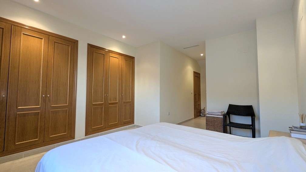 Chambre avec de grands placards intégrés en bois, éclairage encastré au plafond et carrelage aux tons neutres.