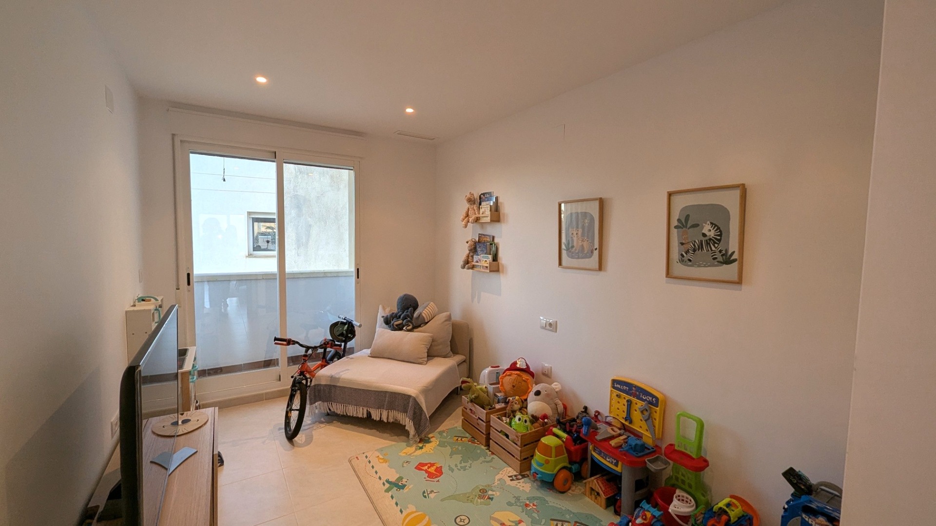 Chambre lumineuse aménagée en salle de jeux, dotée de spots encastrés, d'un sol en carrelage clair et d'un accès direct à la terrasse par une baie vitrée.