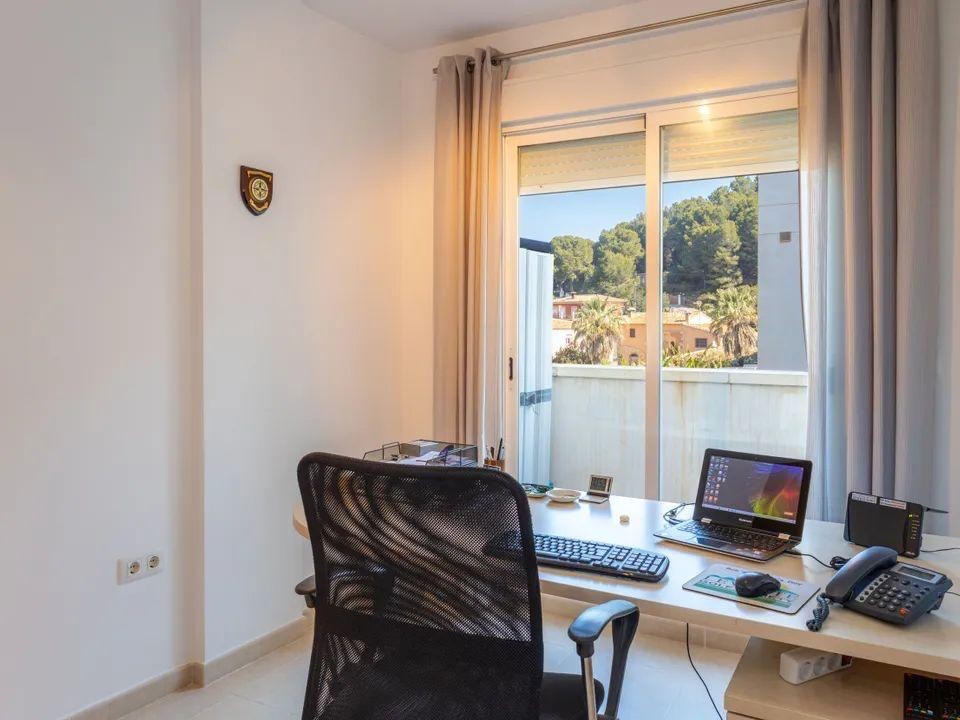 Espace bureau lumineux avec bureau spacieux et porte-fenêtre coulissante offrant une vue dégagée sur les collines boisées environnantes.