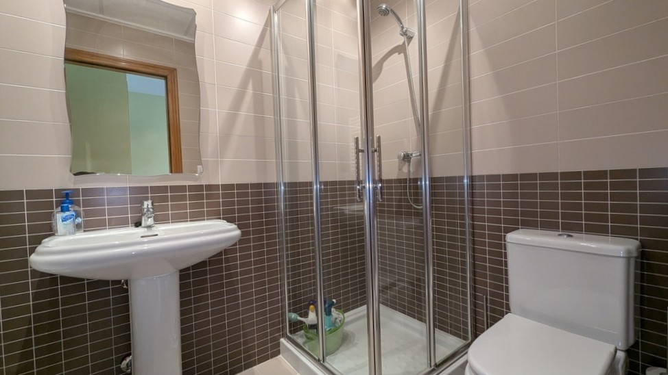 Salle de bain fonctionnelle avec cabine de douche en verre, lavabo sur colonne et carrelage mural bicolore marron et crème.
