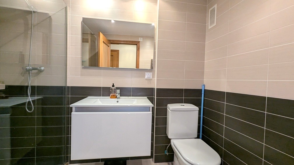 Salle de bains moderne avec carrelage bicolore, meuble vasque suspendu blanc, miroir rectangulaire et douche avec paroi vitrée.