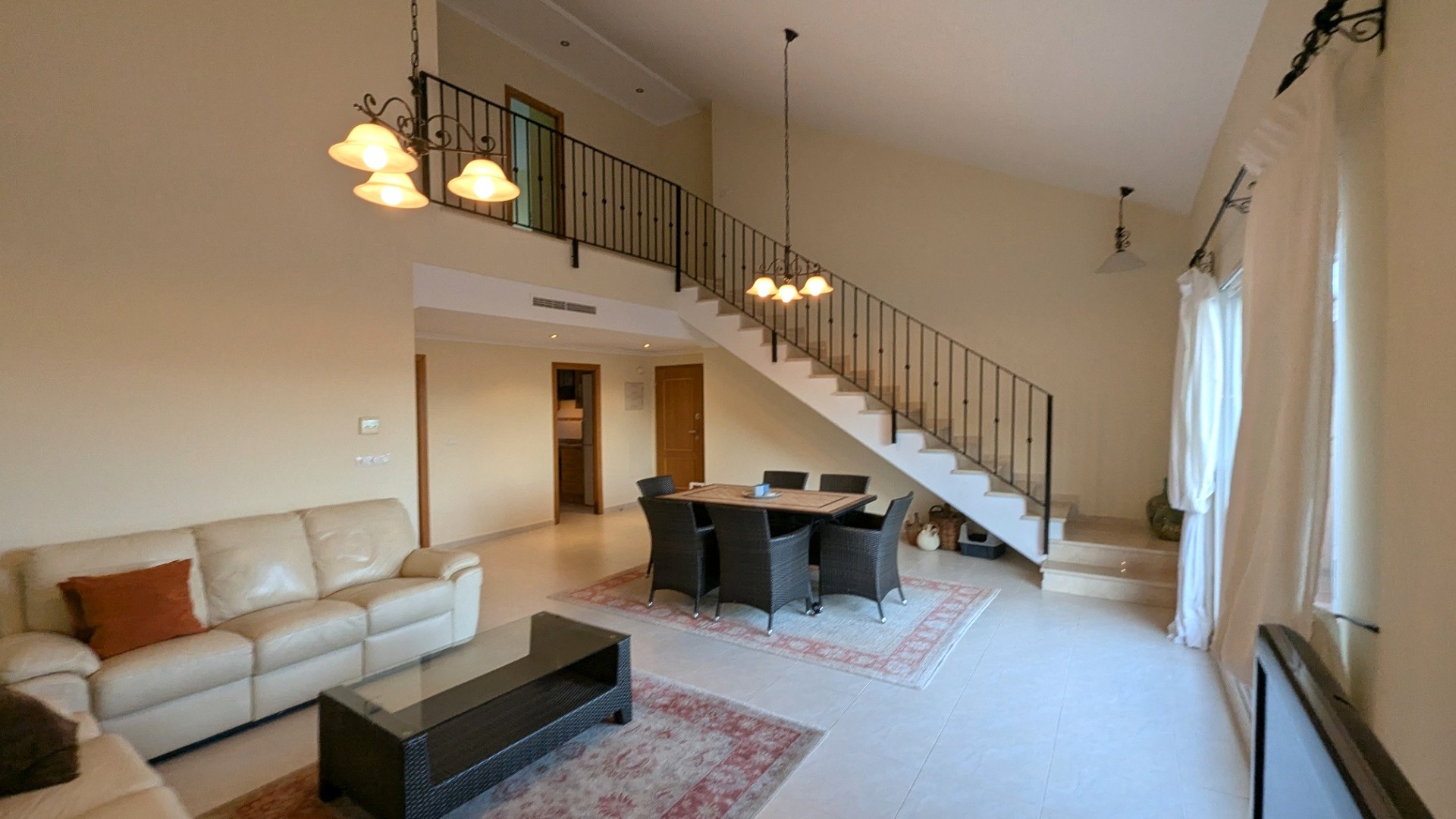 Salon et salle à manger spacieux avec hauts plafonds, escalier en fer forgé et mezzanine surplombant l'espace de vie principal.