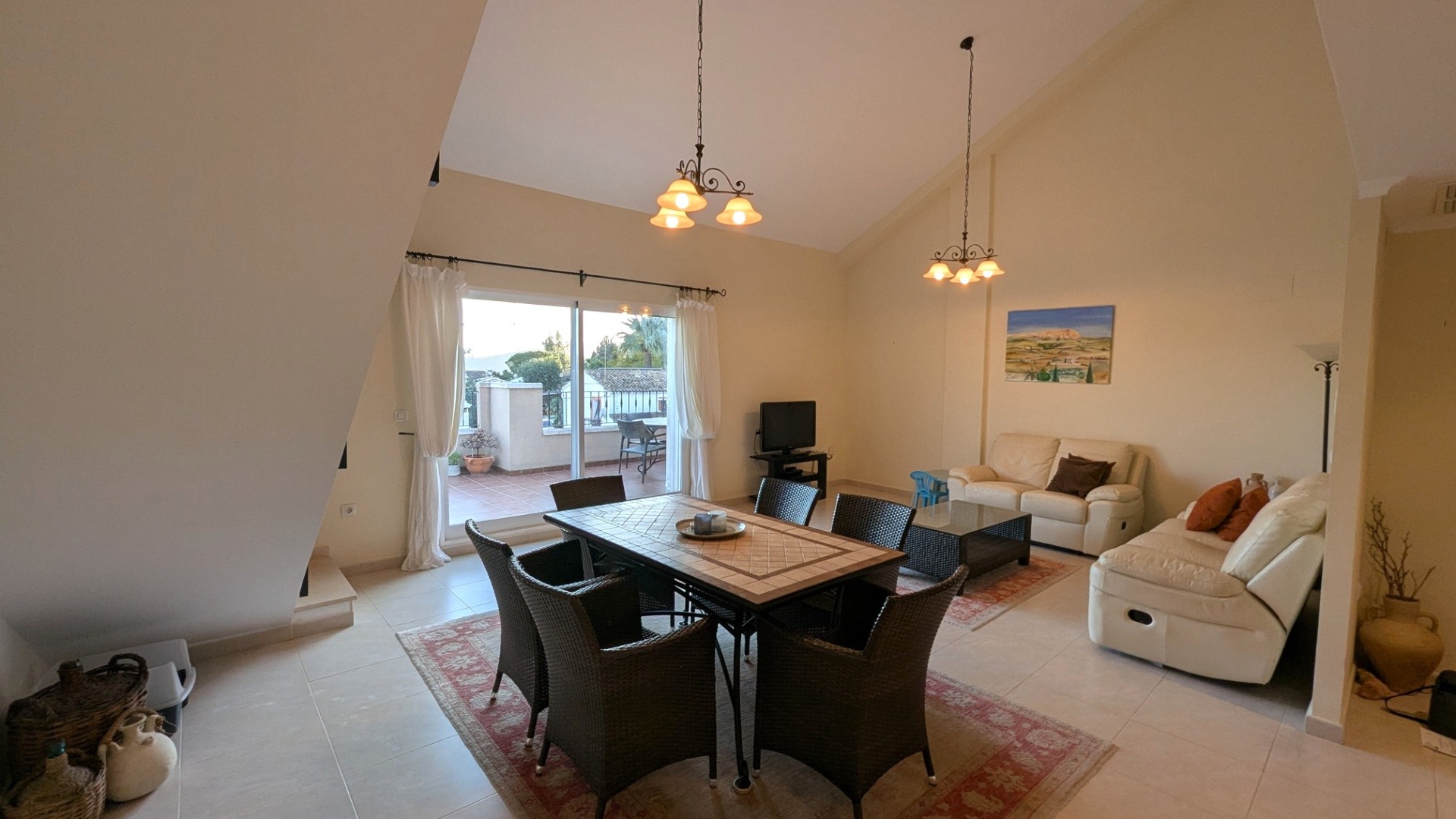 Salon-salle à manger spacieux avec hauts plafonds mansardés, carrelage au sol et accès direct à une terrasse privée par de grandes baies vitrées.