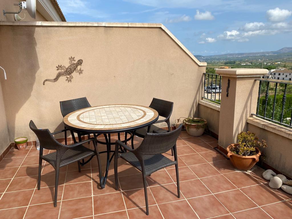 Terrasse carrelée en terre cuite avec table en mosaïque et quatre chaises, offrant une vue dégagée sur la campagne environnante.