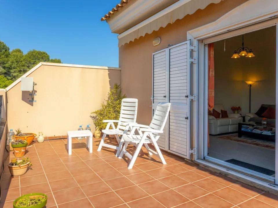 Terrasse extérieure avec carrelage en terre cuite, mobilier de jardin blanc et accès direct au salon par des baies vitrées avec volets blancs.