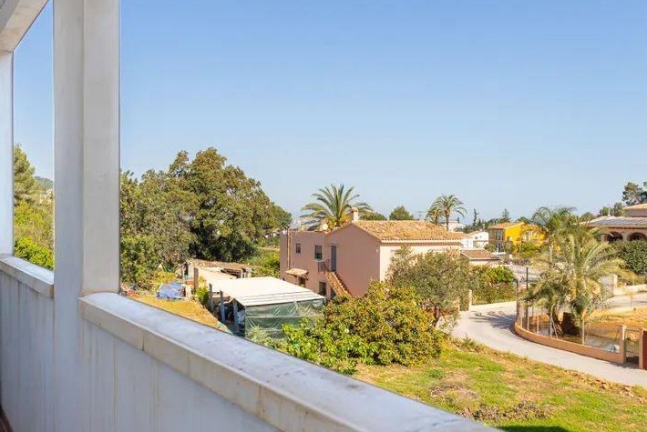 Vue depuis le balcon sur le village de Jesús Pobre, mettant en valeur l'architecture méditerranéenne, les palmiers et le paysage sous un ciel dégagé.