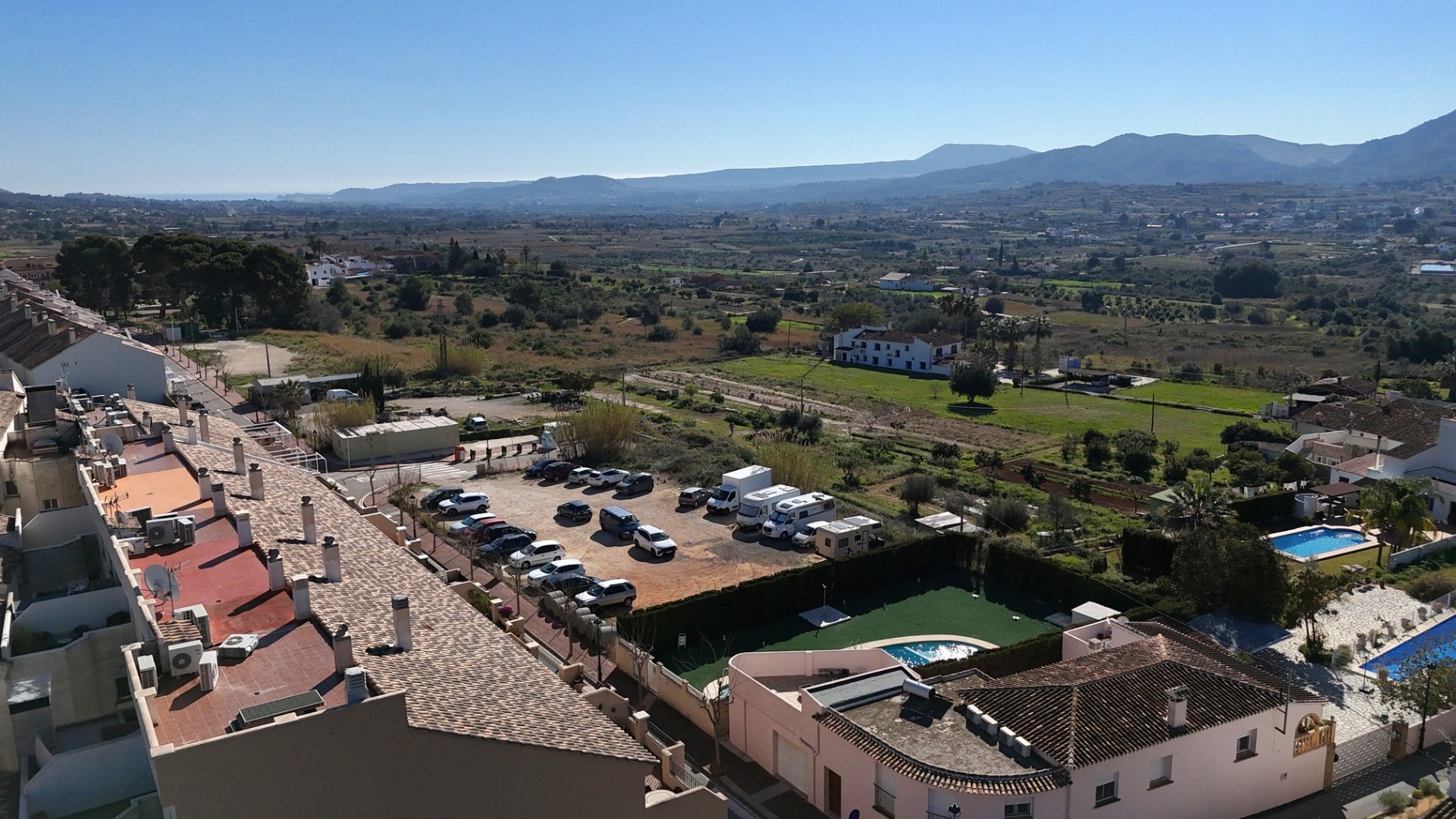 Vue surélevée depuis le penthouse sur la piscine commune, le paysage rural environnant et les montagnes à l'horizon par temps clair.