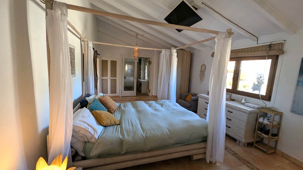 Chambre avec lit à baldaquin en bambou, plafond voûté à poutres blanches et sol en terre cuite. Comprend une télévision au plafond et des rangements intégrés.