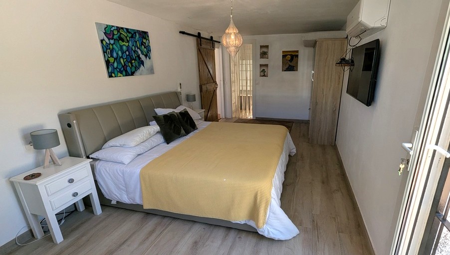 Chambre avec parquet, porte de grange coulissante en bois et lanterne suspendue. Équipée de la climatisation, d'une télévision murale et d'un lit avec tête de lit grise.