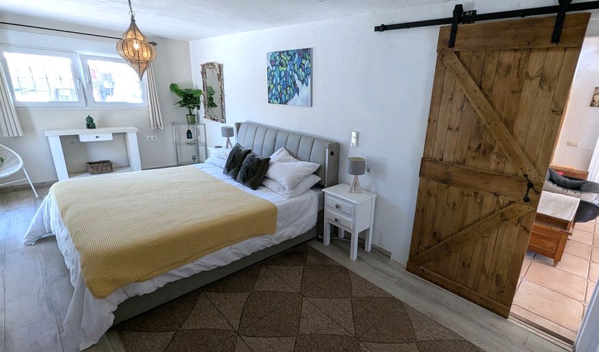Chambre lumineuse avec porte de grange coulissante en bois, tête de lit rembourrée et lanterne marocaine suspendue sur un sol effet bois.