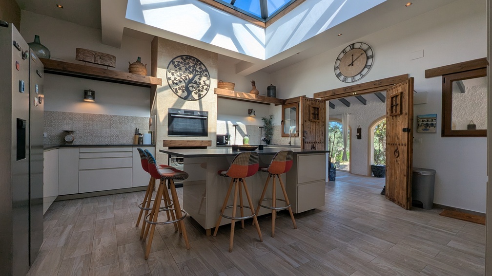 Cuisine moderne dotée d'un puits de lumière vitré, d'un îlot central avec tabourets et de portes en bois traditionnelles ouvrant sur la naya.