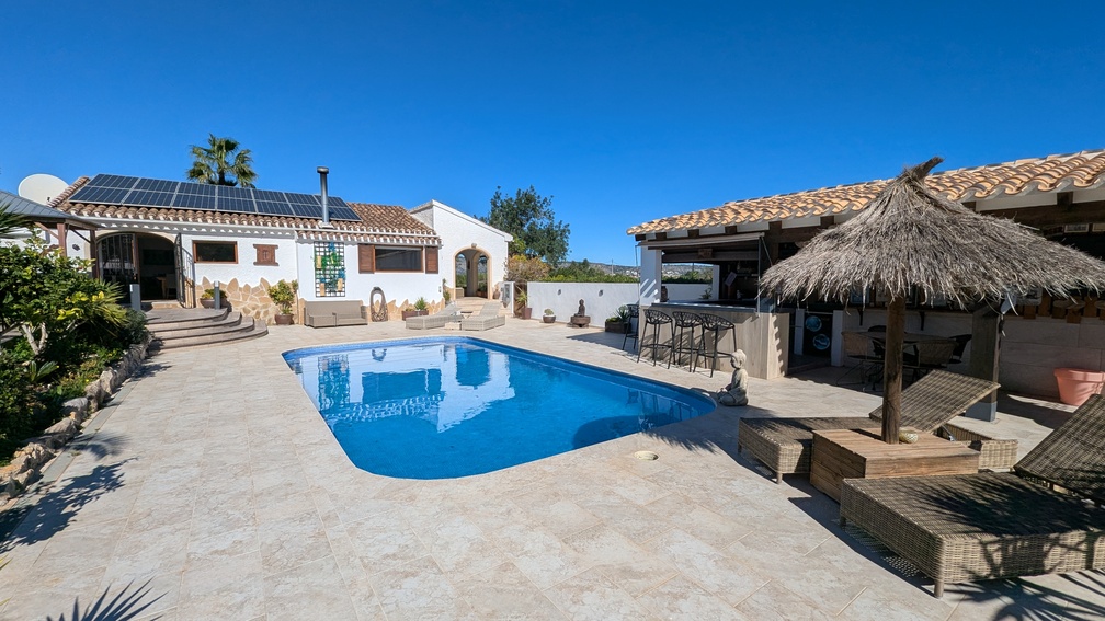 Extérieur de la villa principale avec piscine privée, terrasse en pierre et cuisine d'été équipée, incluant des panneaux solaires et un parasol en chaume.