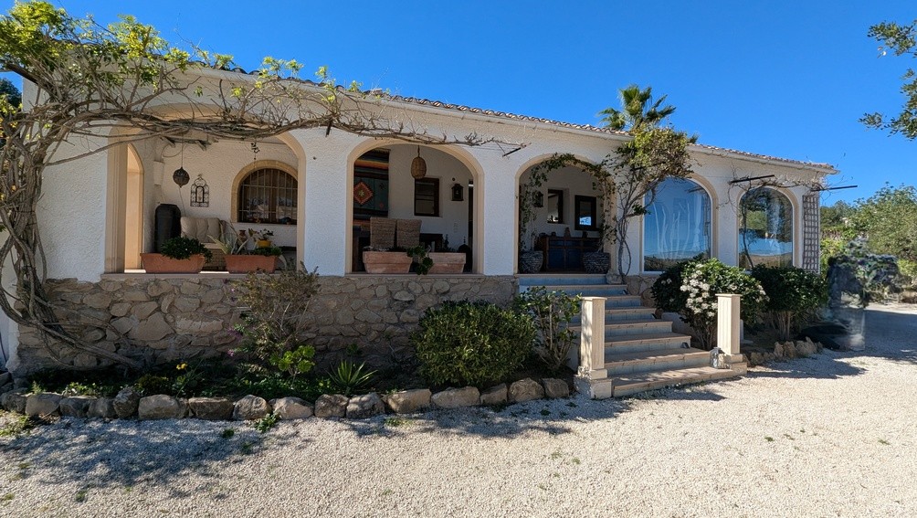 Façade de style finca avec naya à arches traditionnelles, base en pierre naturelle et escalier d'accès bordé de plantes grimpantes.
