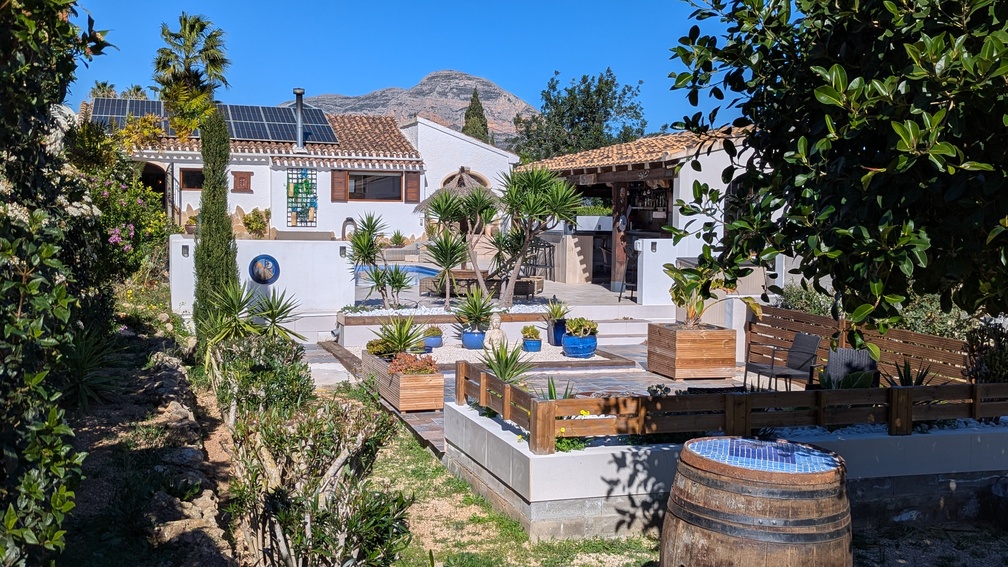 Jardin méditerranéen avec terrasses, cuisine d'été et villa dotée de panneaux solaires, offrant une vue dégagée sur la montagne Montgó.