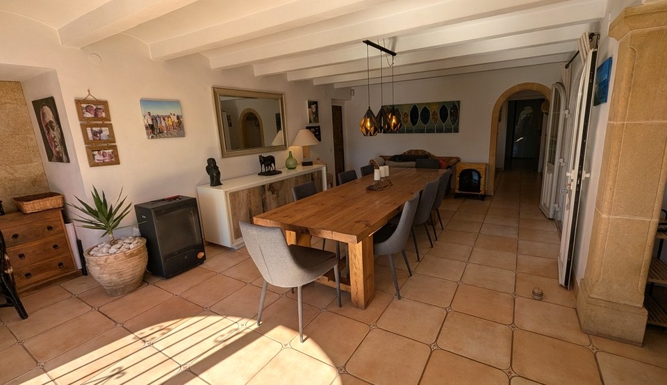 Salle à manger spacieuse avec une grande table en bois massif, sol en terre cuite et plafond à poutres blanches. Un pilier en pierre Tosca et une arche soulignent le style traditionnel de la finca.