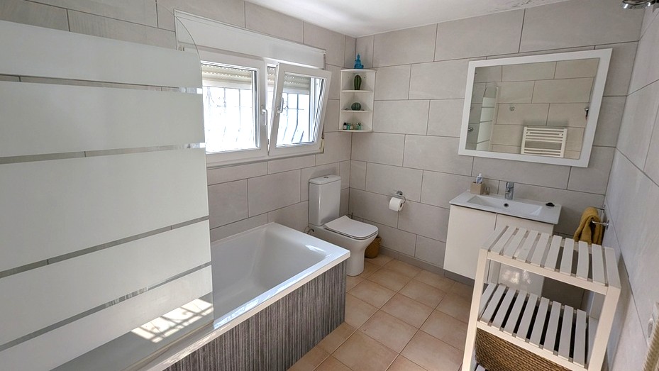 Salle de bain moderne avec baignoire intégrée, paroi en verre dépoli, meuble vasque blanc et carrelage mural grand format aux tons neutres.