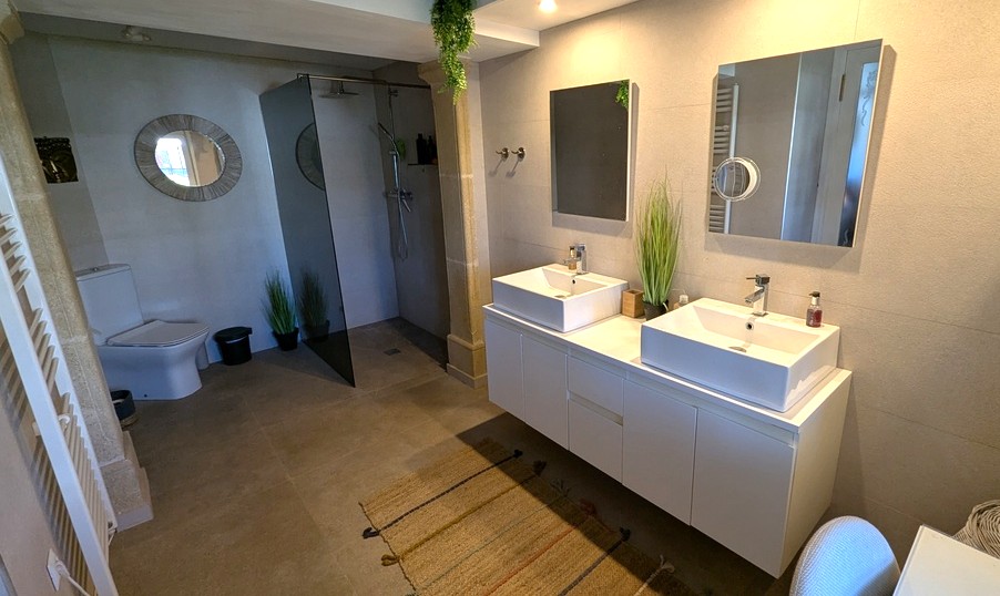 Salle de bains contemporaine avec double vasque, douche à l'italienne à paroi fumée et carrelage en pierre naturelle aux tons sobres.