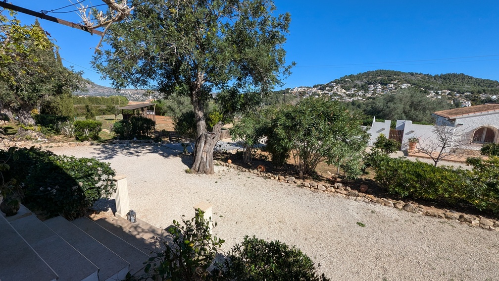 Vue surélevée de l'allée en gravier et des jardins méditerranéens, avec des oliviers matures et une vue sur les collines environnantes et les quartiers de Jávea.