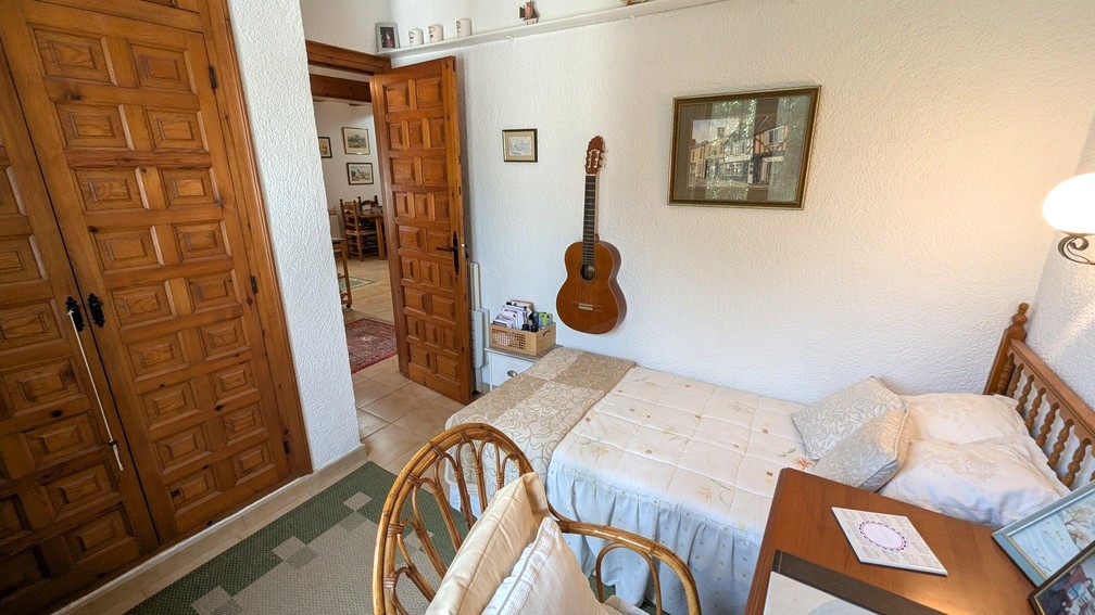Chambre avec lit simple, placards intégrés en bois de style traditionnel et murs texturés. Une porte ouverte donne sur le couloir et les pièces de vie.