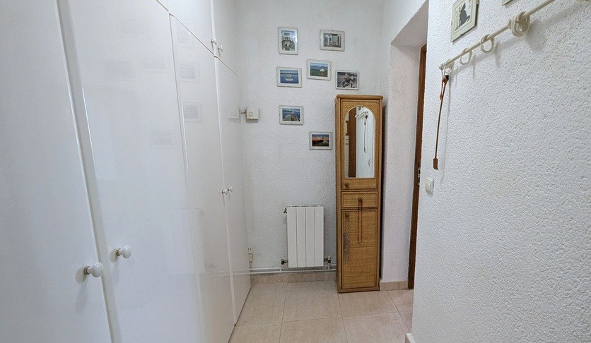 Couloir ou zone de dressing avec de grands placards intégrés blancs, un meuble de rangement en osier avec miroir et un radiateur mural.