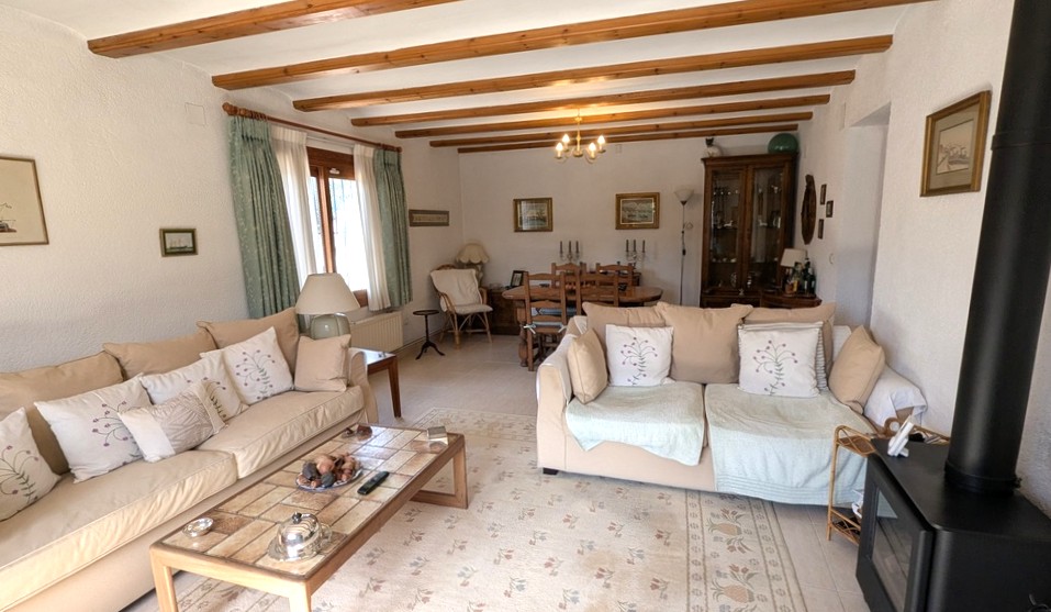 Espace salon et salle à manger traditionnel avec poutres en bois apparentes, poêle à bois noir et mobilier classique aux tons neutres.
