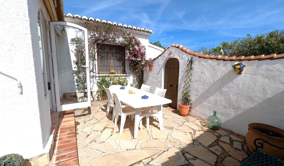 Patio extérieur privé avec dallage en pierre naturelle, mobilier de repas blanc et architecture méditerranéenne traditionnelle aux murs blancs et toits de tuiles.